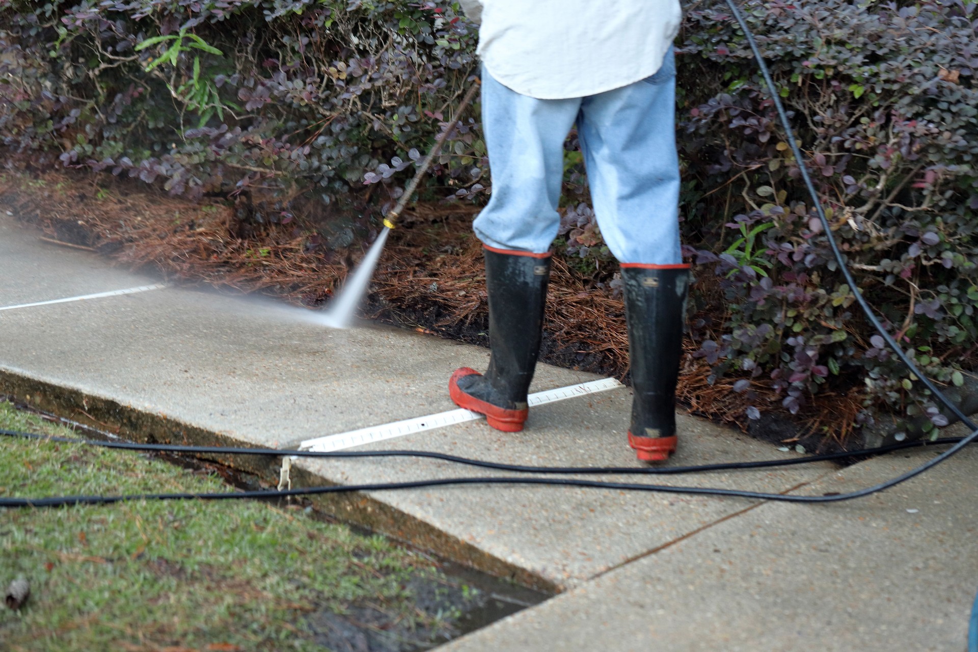 Worker pressure washing conrete sidewalk to clean it